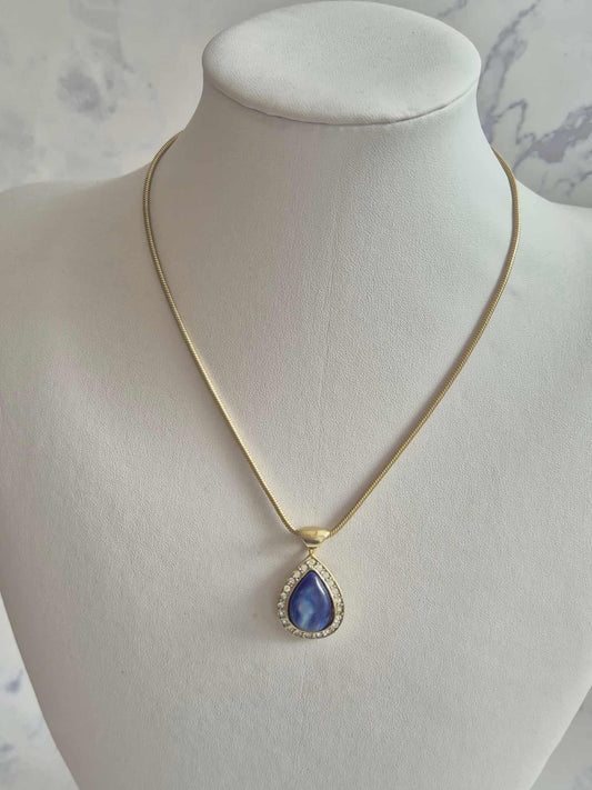 Aukso spalvos kaklo papuošalas su mėlynu lašo formos akmeniu